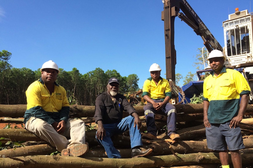 A group of men in work gear sitting on a pile of logs.