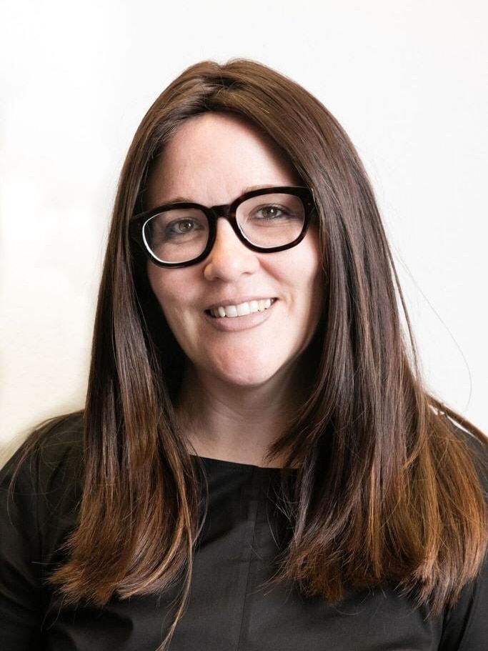 Tamar Krebs, a woman with long, brown hair wearing black-framed glasses and a black top. 