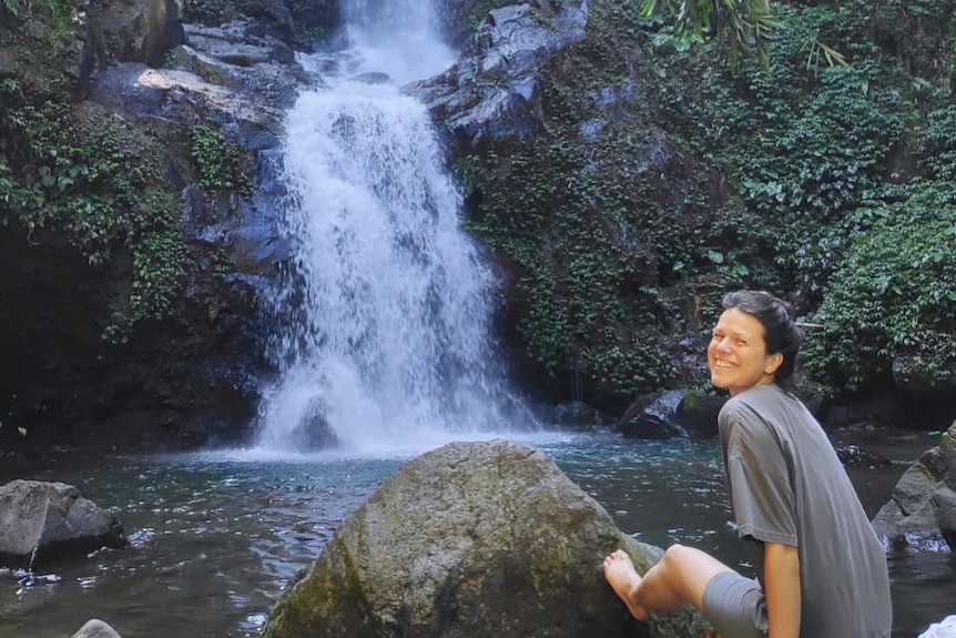 A women sits on rocks in front ofa waterfall smiling. 