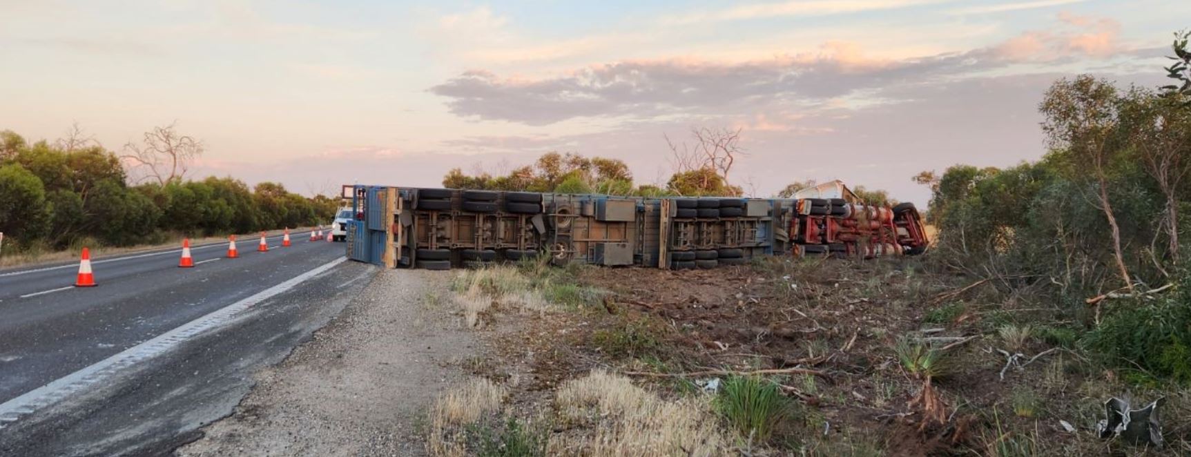 A truck laying on its side on the side of a highway. 