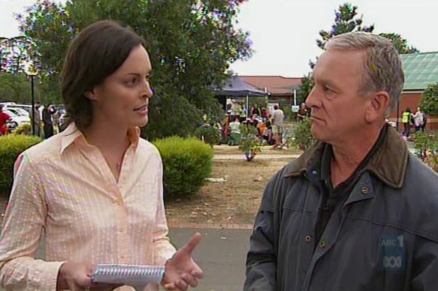 Still image of Cowan talking to Henderson standing in front of people outside community centre.