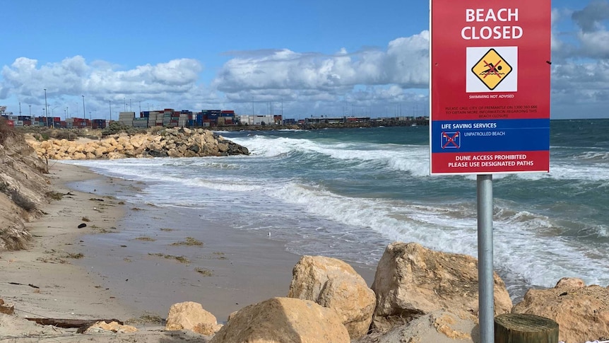 A beach closed sign at a Fremantle beach with the port in the background.