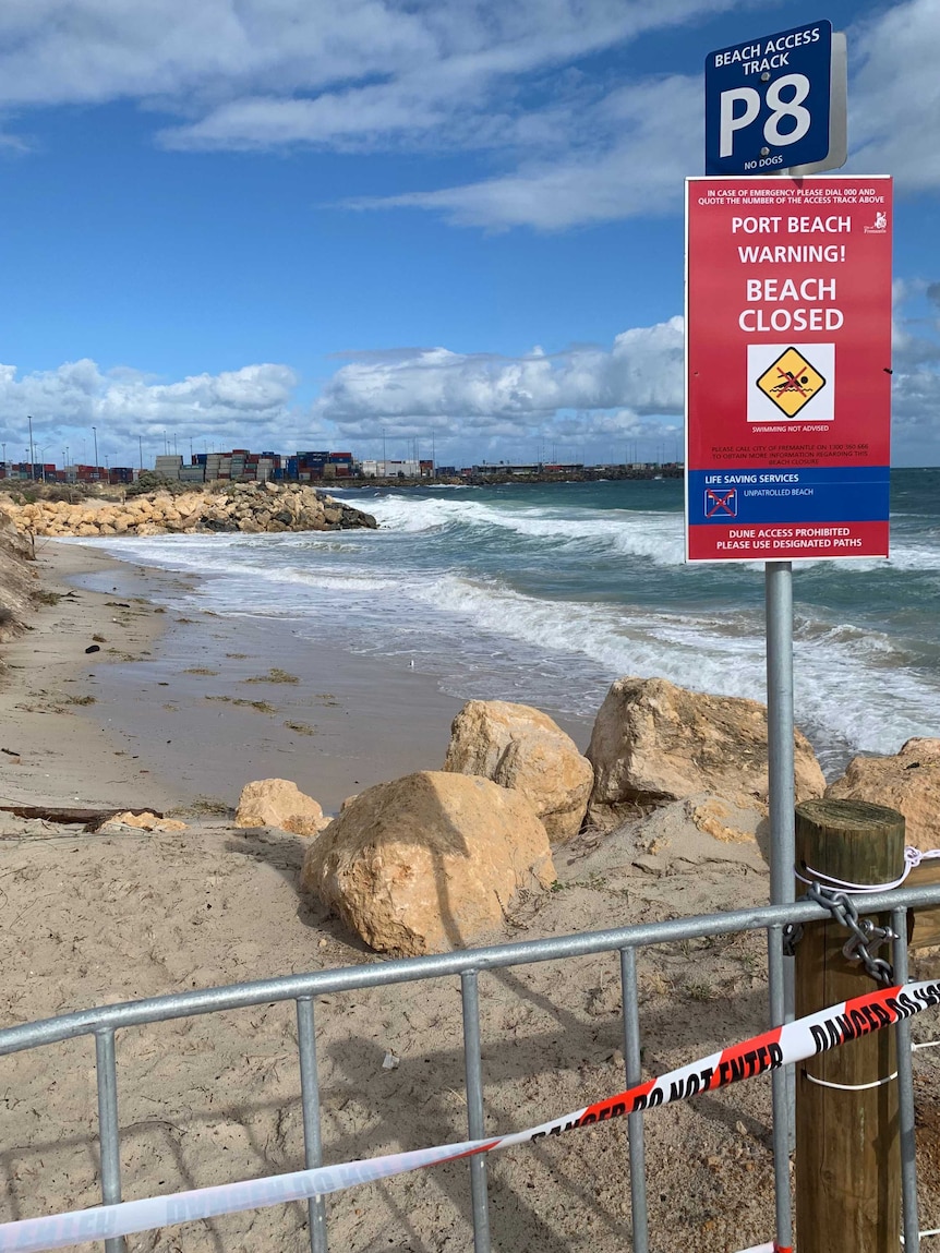 A beach closed sign at a Fremantle beach with the port in the background.