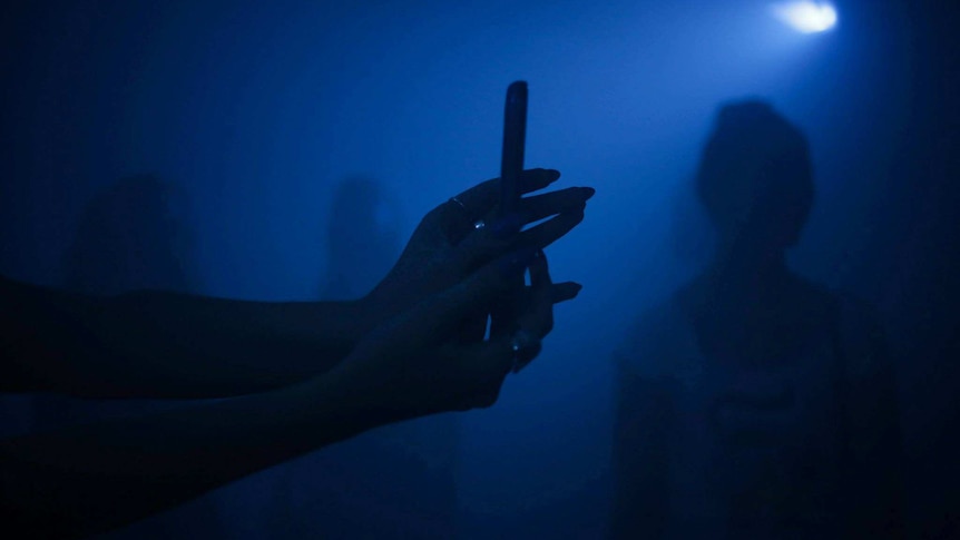 A silhouetted pair of hands inside a darkened, blue room.