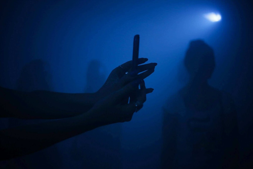 A silhouetted pair of hands inside a darkened, blue room.