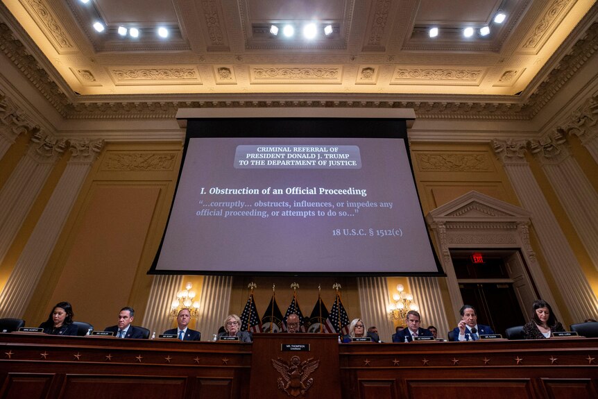 "Criminal Referral Of President Donald J. Trump To The Department Of Justice" is displayed on a screen behind a row of people