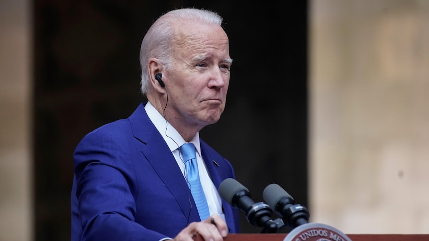 President Joe Biden standing at a lectern with an ear piece. 