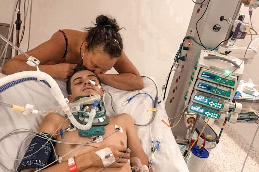 Mother kisses son on forehead in hospital as he sleeps attached to many wires and pipes