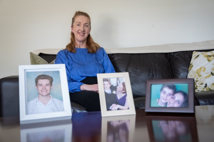 woman in blue shirt smiling behind pictures of her son