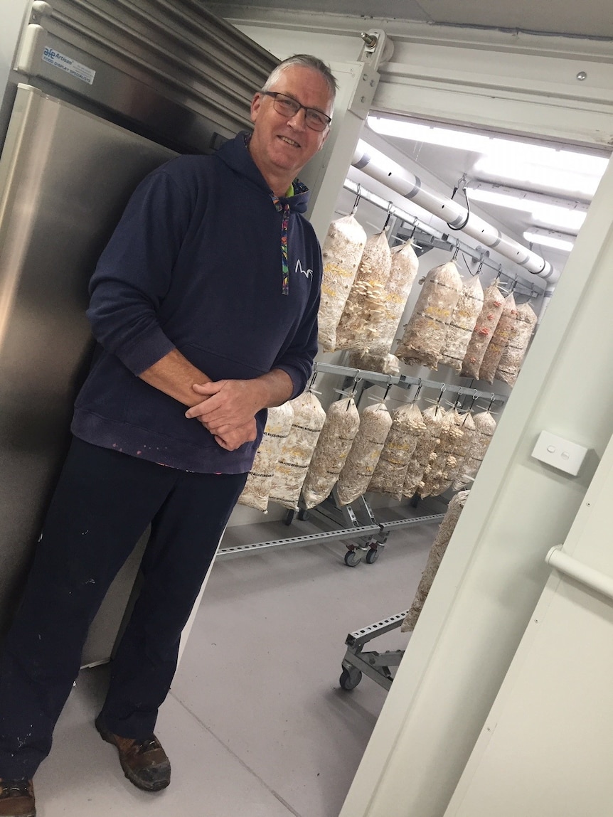 A man stands smiling with bags of fungi in the background.