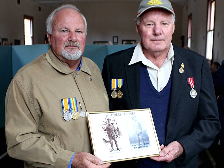 Terry and Robert Javens pose for a picture holding a photo or their ancestors.