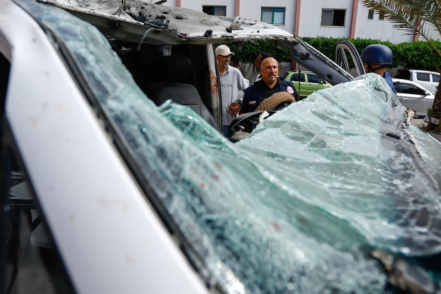 A man concerned man observes the shattered windscreen of an ambulance.