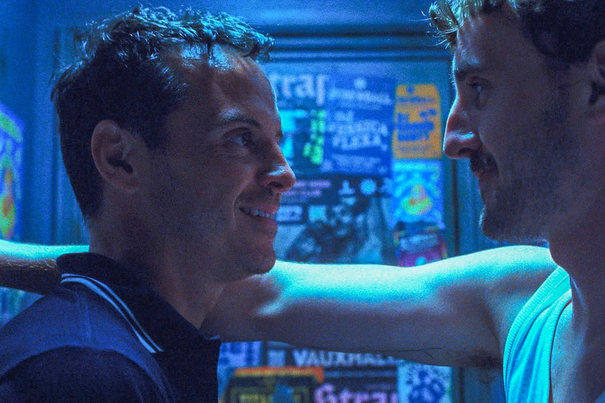 Mescal puts his arm over Scott's shoulder, the two looking at each other in a blue-lit nightclub cubicle donned with posters.