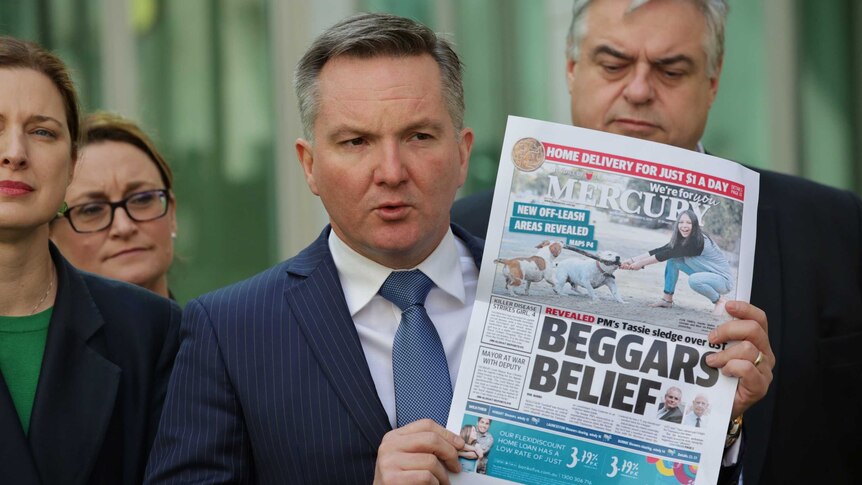 Chris Bowen holding a copy of the Hobart Mercury with the headline Beggars Belief as Tasmanian colleagues stand behind