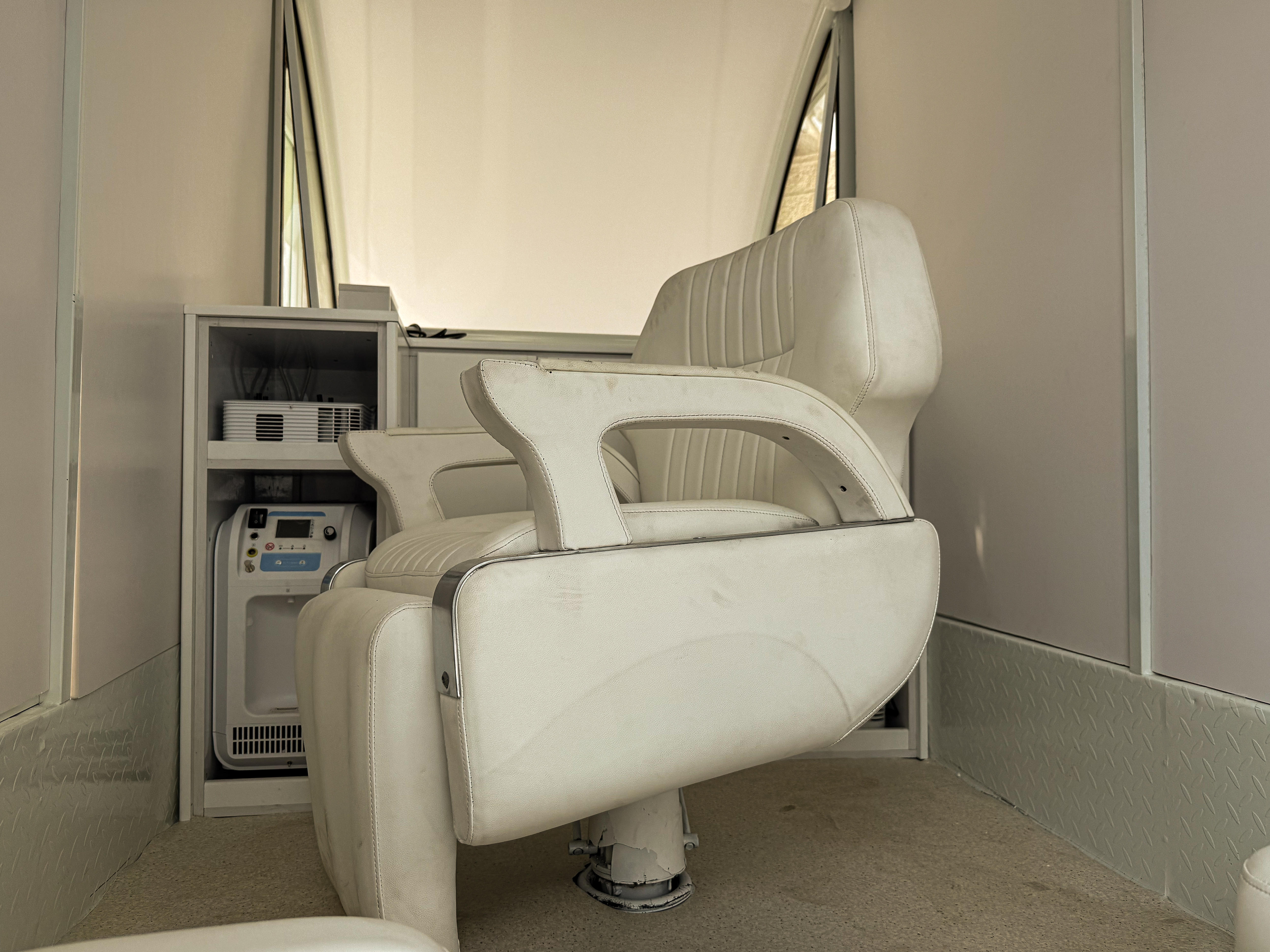 medical chair with arm and foot rests attached to the floor of popemobile. a cupboard behind it contains medical devices.