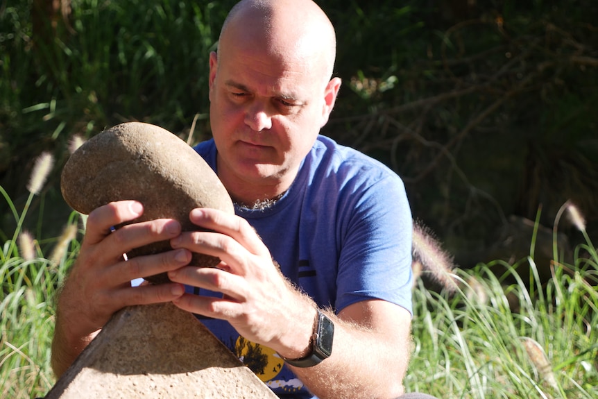 A man stares intently as he places a rock on the point of another one. 