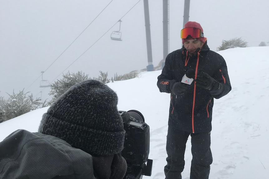 A man stands in snow next to a camera.