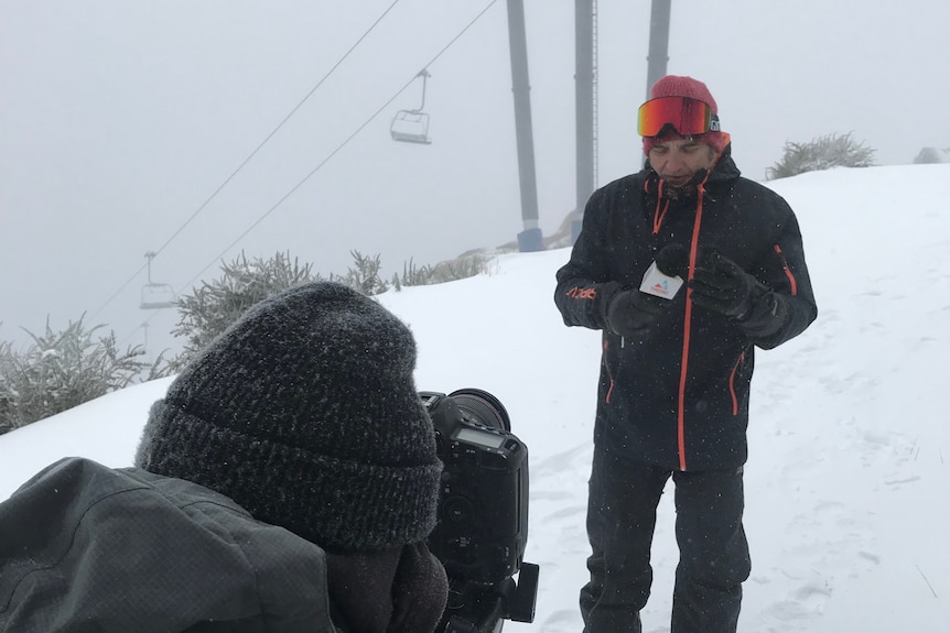 Un hombre se para en la nieve junto a una cámara.