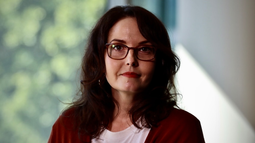 a woman in a red cardigan and glasses looking into the camera