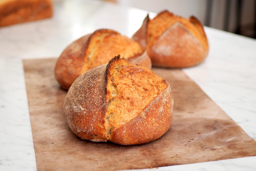 Three loaves of bread sit on a bench