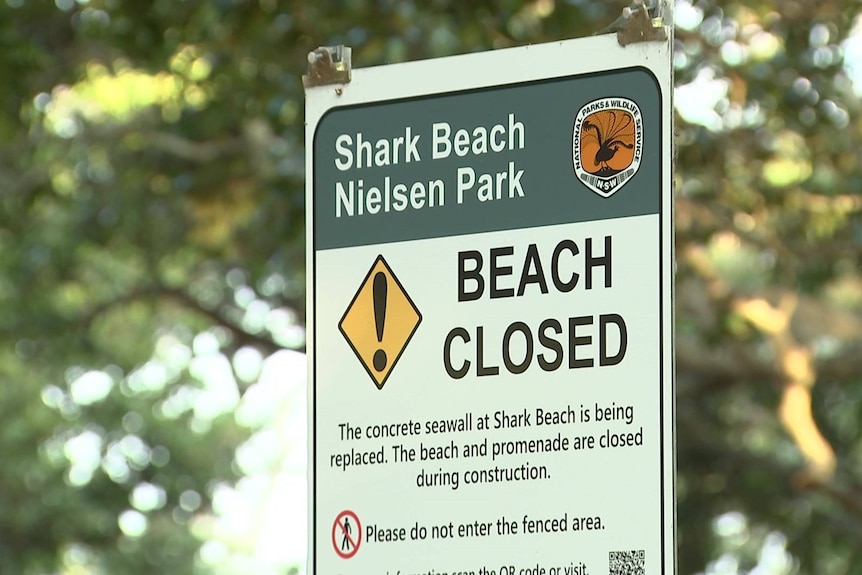 a sign at a sydney harbour beach that reads beach closed as repair work continues to a broken seawall