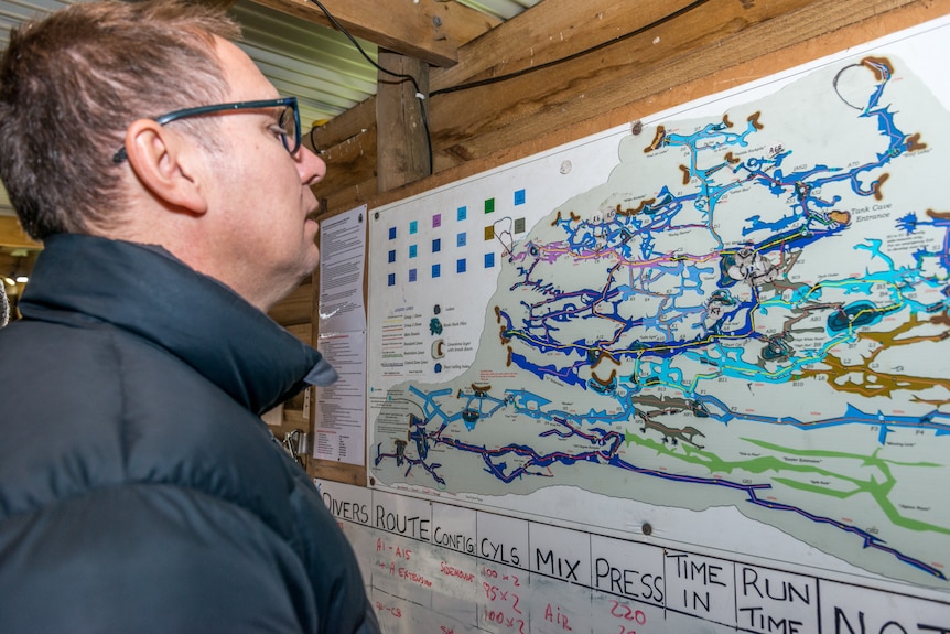 A man in a puffer jacket and glasses looks at a large laminated map of cave channels.