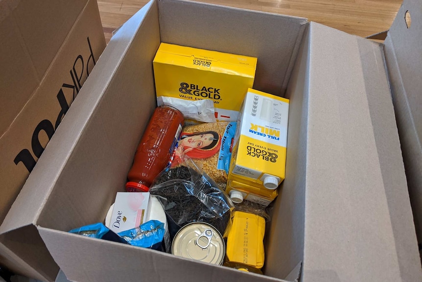 An open cardboard box filled with long-life milk, pasta sauce, cereal and rice.