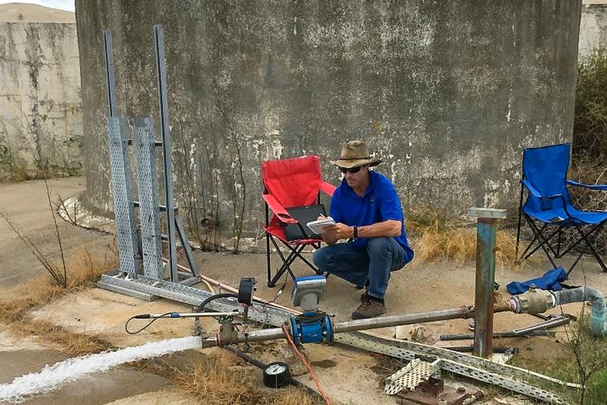 A man kneels near a concrete water reservoir, taking notes.