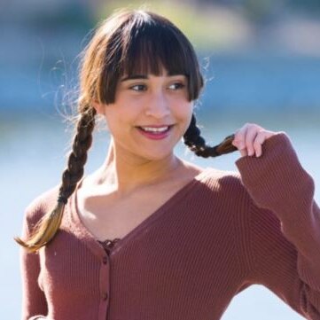 girl with a fringe and plaits looking to one side smiling with a plait in one hand