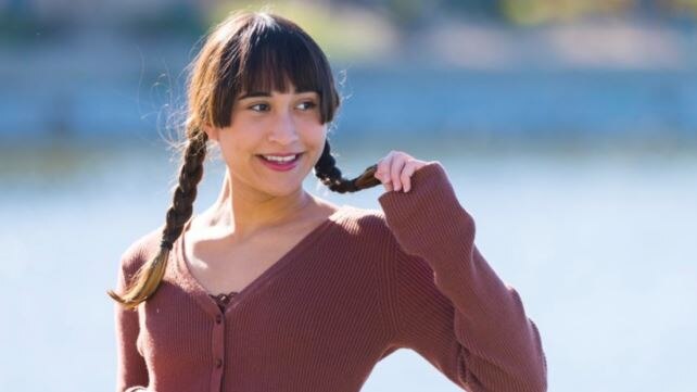 girl with a fringe and plaits looking to one side smiling with a plait in one hand