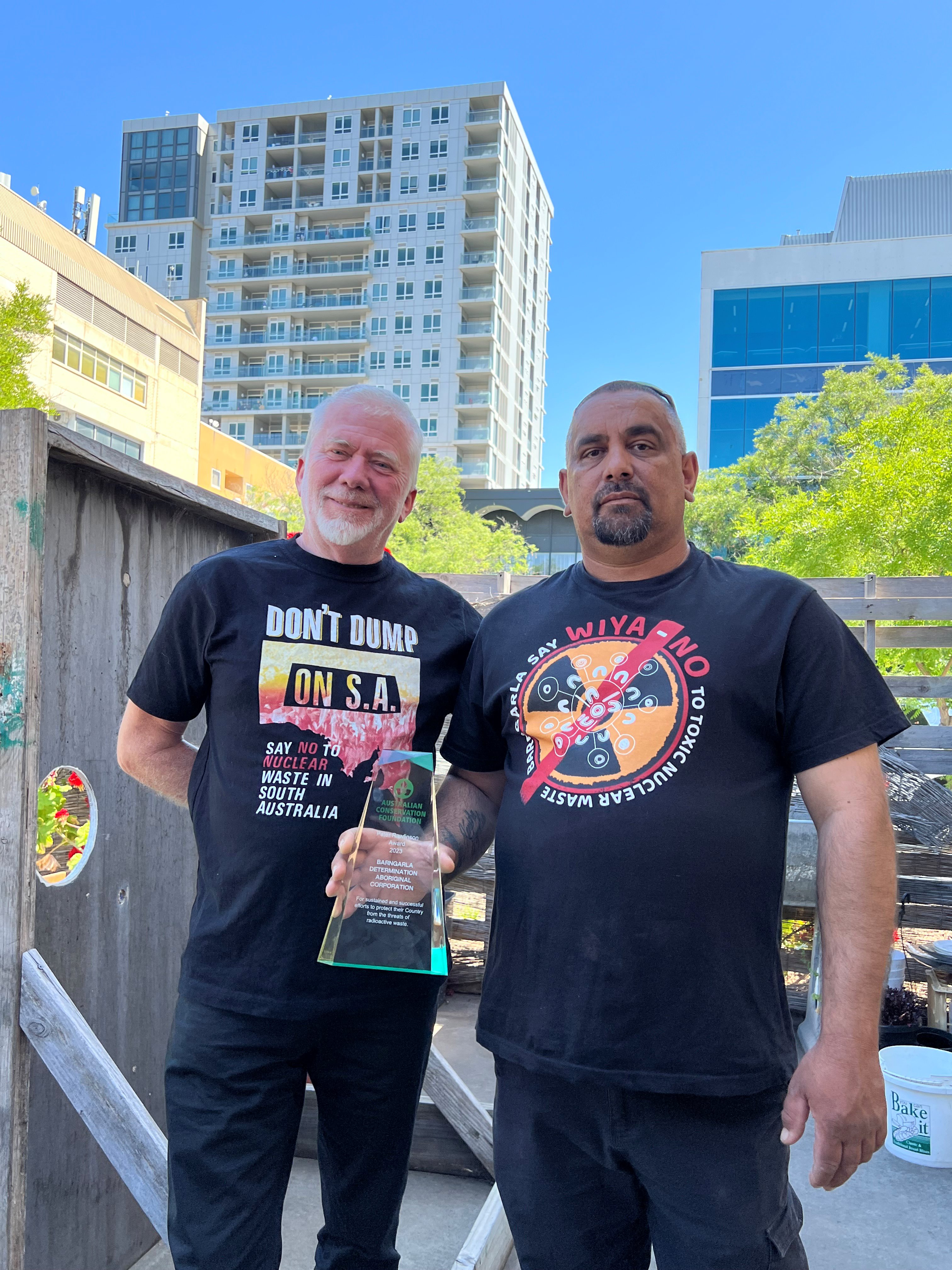 Dave Sweeney and Jason Bilney stand side by side in tshirts reading "don't dump on S.A", Jason holds the award