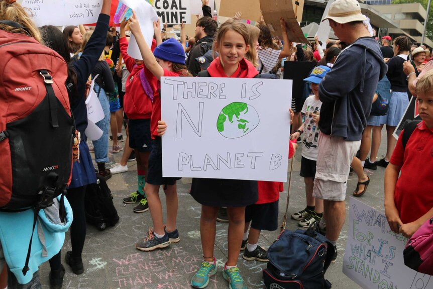 A young girl stands with a protest sign reading 'There is no Planet B'.