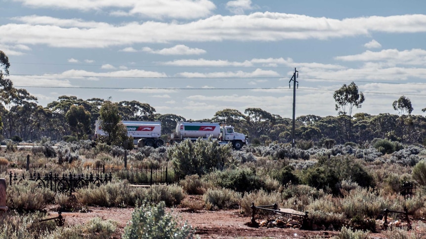 Image of a small country graveyard with a truck driving along a road in the background.