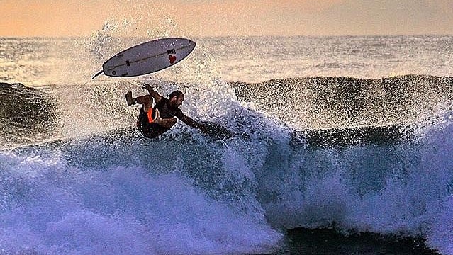 A surfer and his board separate as they fly off the top of a wave during a wipe out.