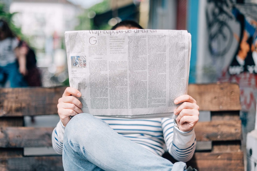 A man reads a folded broadsheet newspaper, depicting the difficulties in navigating the news.