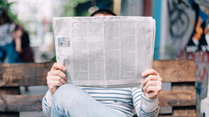 A man reads a folded broadsheet newspaper, depicting the difficulties in navigating the news.