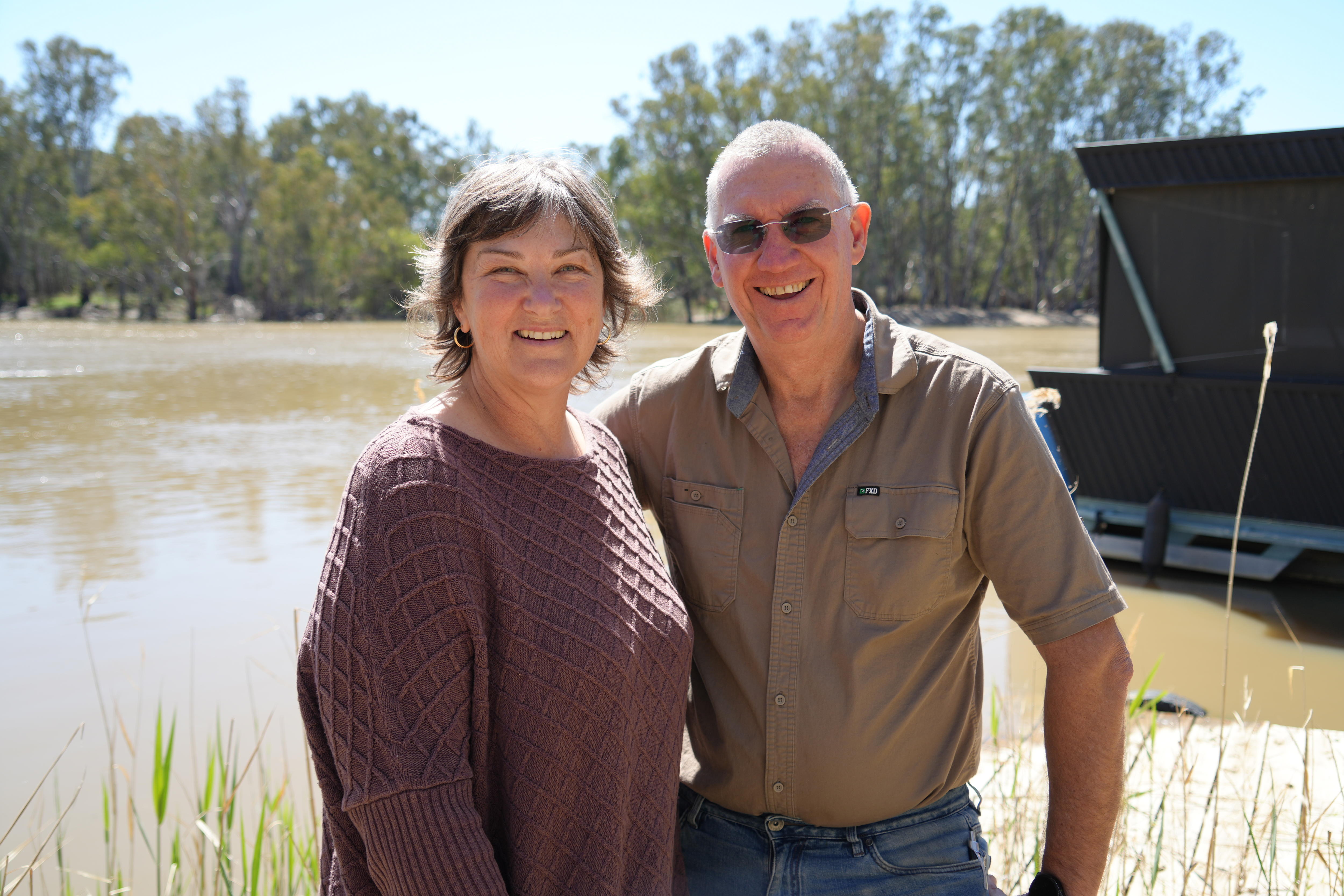 A man and a woman standing in front of the River Murray smile.