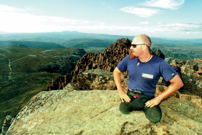 A man in his early thirties with both legs amputated sitting on the top of Cradle mountain