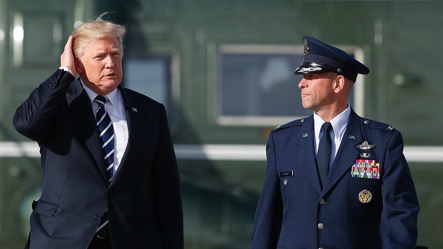 Donald Trump walks with a man in formal military uniform.