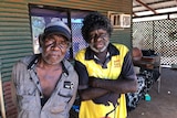 Two Indigenous men standing on the verandah of a house.