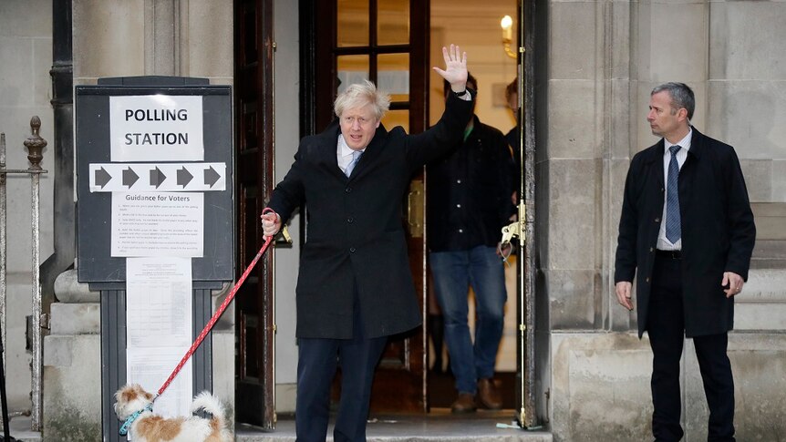 A man waves as he walks a dog on a leash and walks out of a polling station