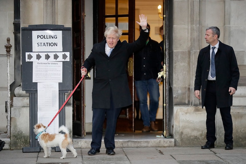 A man waves as he walks a dog on a leash and walks out of a polling station