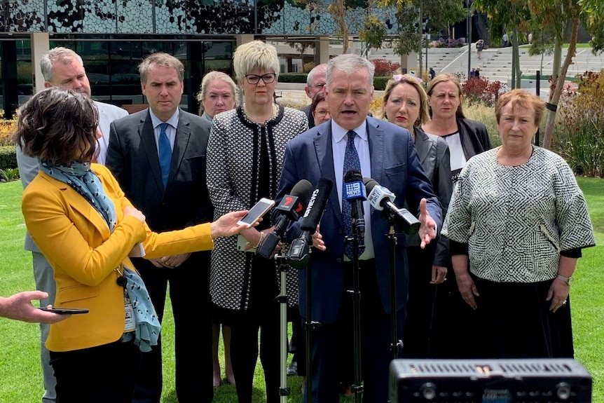 A man speaks into microphones while other people stand behind him