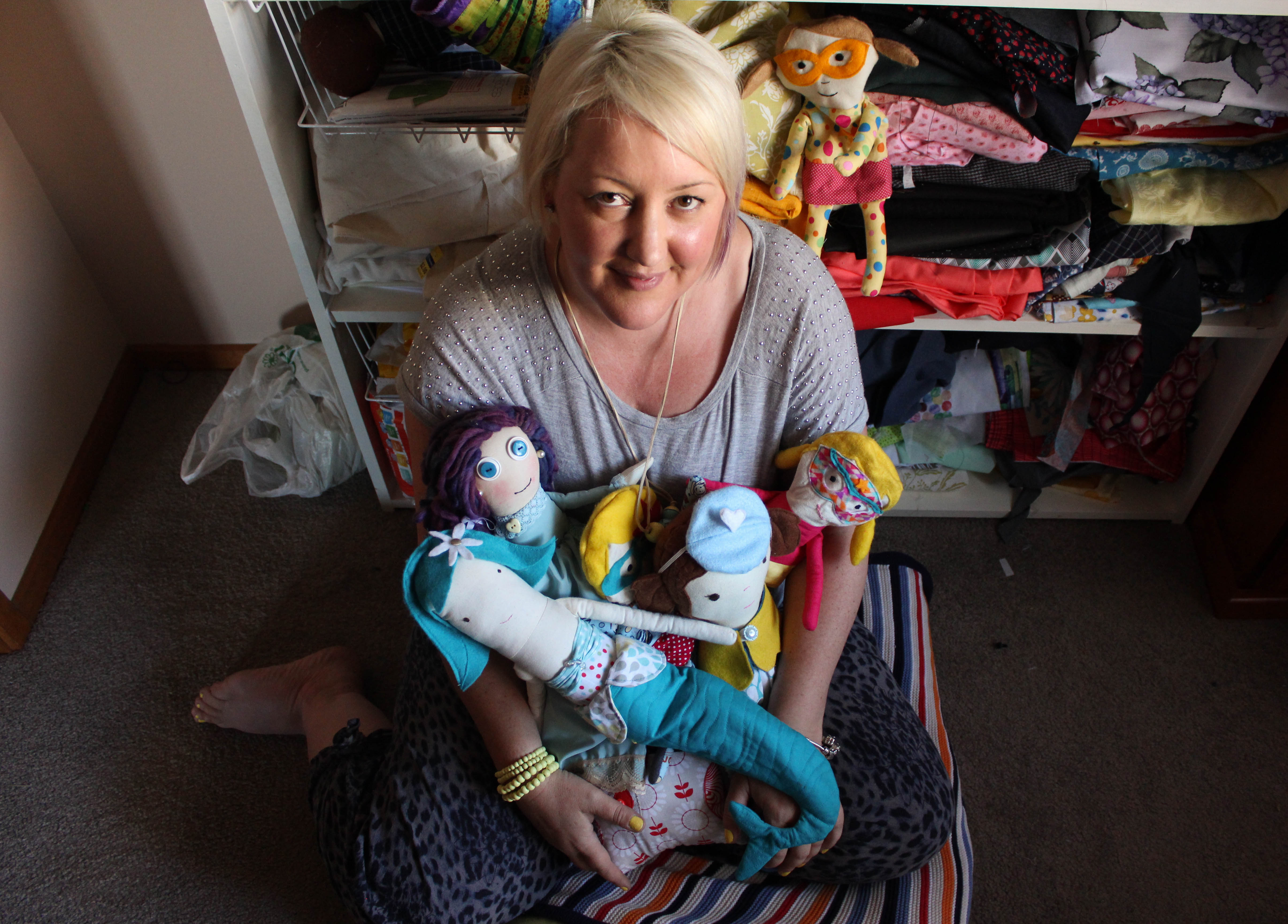 A woman sitting on the floor holding hand-made dolls.