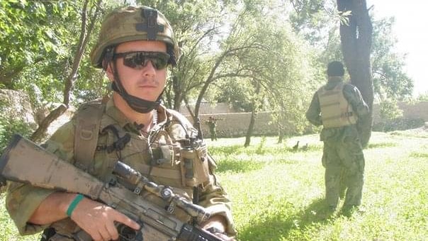 Phillip Thompson, dressed in army camo gear, stands holding gun. He's wearing a helmet and sunglasses