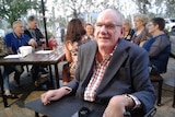 Des Ryan, seated in wheelchair, in front of the Accessible Pub Crawl team sitting round an outdoor pub table.