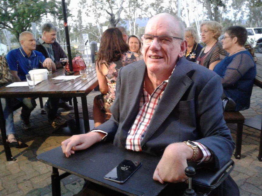 Des Ryan, seated in wheelchair, in front of the Accessible Pub Crawl team sitting round an outdoor pub table.