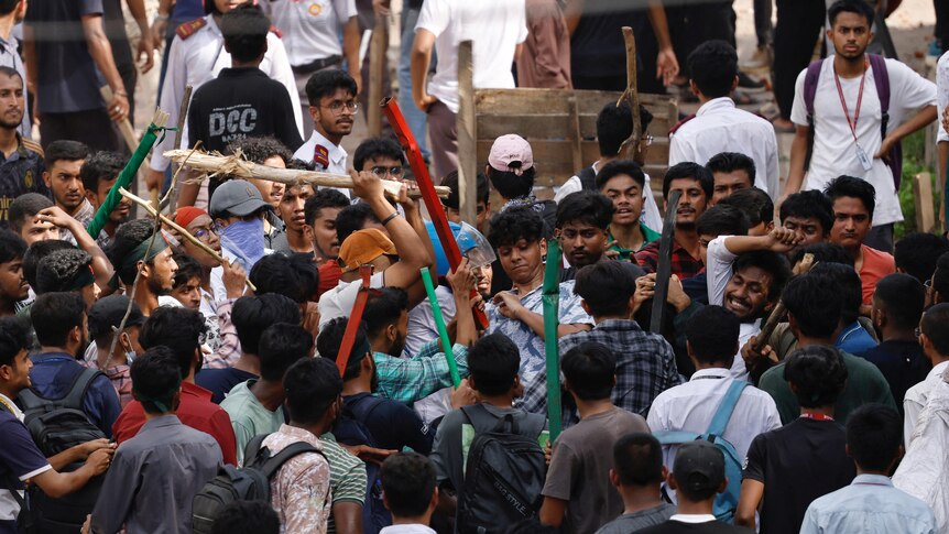 A large mob of people wielding sticks and batons attacks each other 