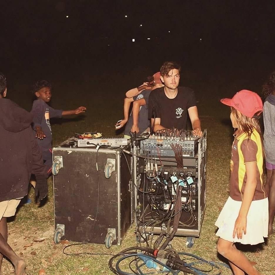 A sound engineer stands at a sound box at an outdoor gig in the evening.