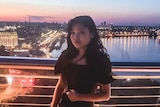 Maria Nam poses for a photo in Kyiv with a view of a river and the sun setting in the background.